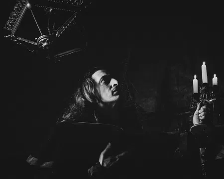 Black and white photo of a person holding a candelabra with burning candles in a dark, gothic setting.
