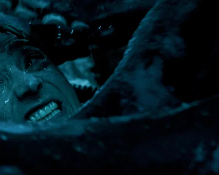 Close-up of a man's tense face underwater surrounded by tentacles in dark blue lighting.