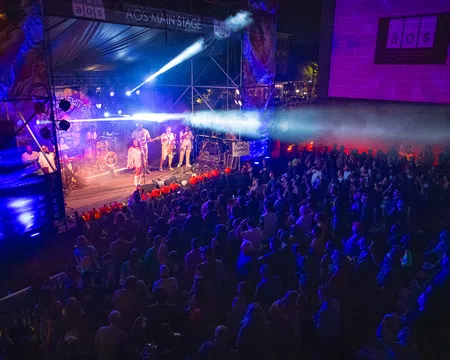Live band performing on AOS Main Stage with colorful lights and large crowd at night concert event.