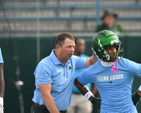 Football coach instructing player wearing green helmet and blue Roll Wave shirt during practice session