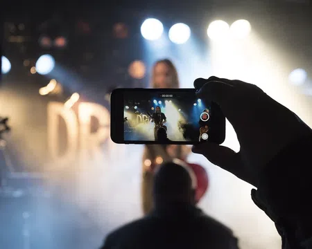 Person recording a live music performance on smartphone with stage lights and smoke effects in background