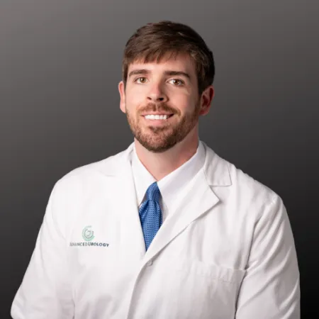 Smiling male doctor in white coat and blue tie against gray background, representing advanced urology care.