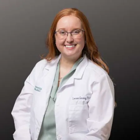 Smiling female healthcare professional with red hair wearing glasses and a white lab coat against a dark background