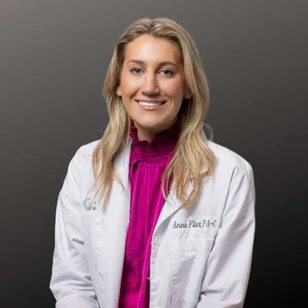 Smiling female medical professional in white coat with pink blouse against a dark gray background.
