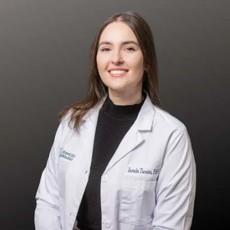 Smiling female doctor in white lab coat against gray background, professional healthcare portrait.