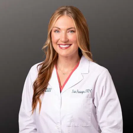 Smiling female healthcare professional with long hair wearing a white lab coat against a gray background