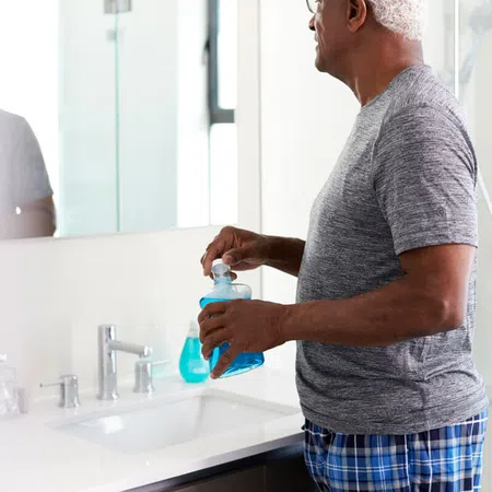 Senior man holding a bottle of cleaning solution in a modern bathroom mirror setting.