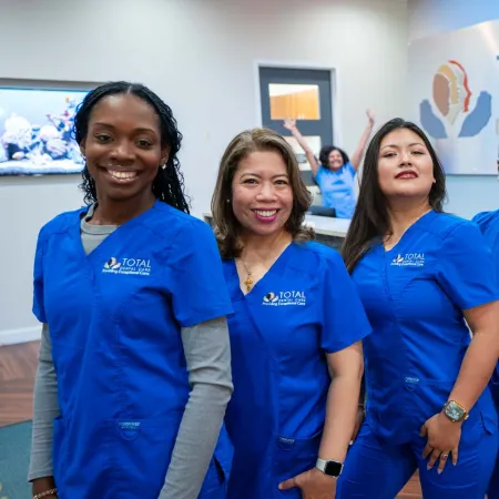 Diverse dental care team in blue scrubs smiling confidently inside Total Dental Care clinic.