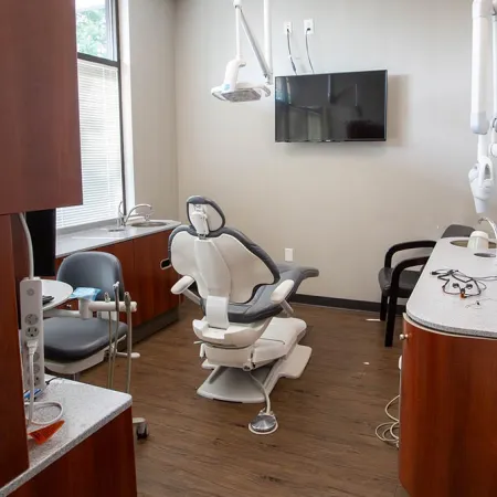 Modern dental clinic room with dental chair, TV, equipment, and wooden cabinets under natural light
