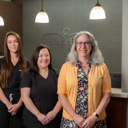 Dental team of three women and one man smiling in office with Westlake Hills Dentistry sign behind them.