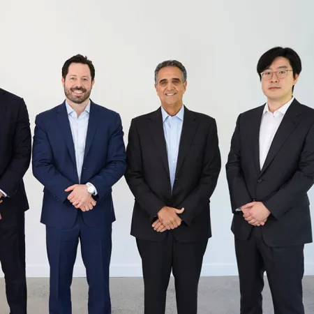 Five professionals in suits standing together, smiling, in a modern office environment.