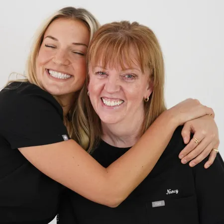 Two smiling women in black shirts hugging, showcasing a moment of joy and camaraderie.