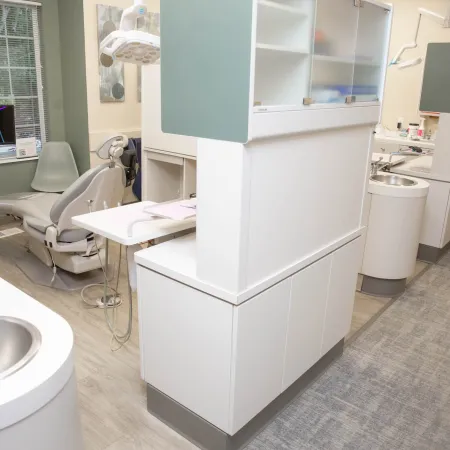 Modern dental clinic interior with dental chair, equipment, sinks, and cabinets in a clean, bright space.