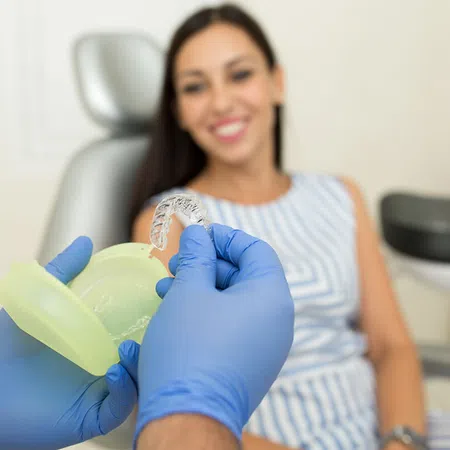 A patient smiles while receiving dental care, holding an orthodontic aligner in hand.