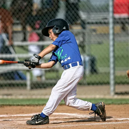 Young baseball player in blue jersey swinging bat during a game on a sunny day at the field