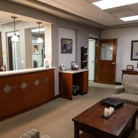 Modern office waiting area with wooden reception desk, armchairs, coffee table, and neutral decor.