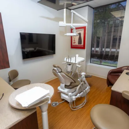 Modern dental office with dental chair, equipment, TV, and seating in a clean clinical setting.