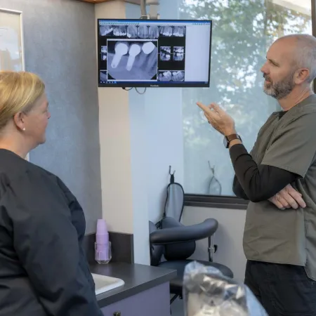 Dentist explains dental X-rays to a female patient in a modern clinic with large windows and natural light.