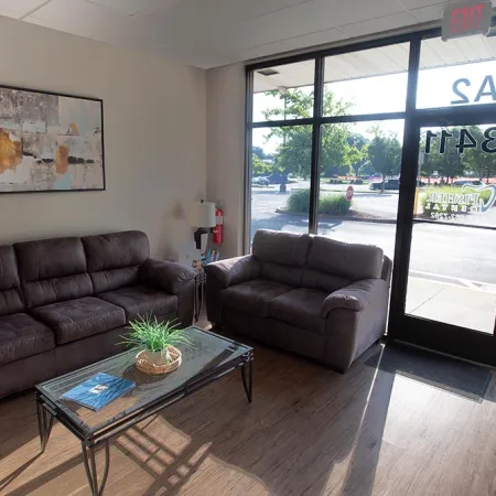 Cozy waiting room with two brown sofas, glass coffee table with plant, and large windowed door to outside.