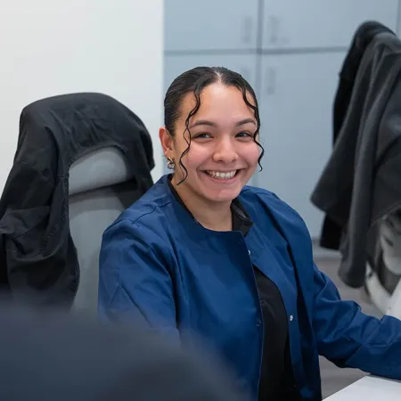 Smiling woman in blue jacket sitting at desk and engaging in conversation in modern office setting
