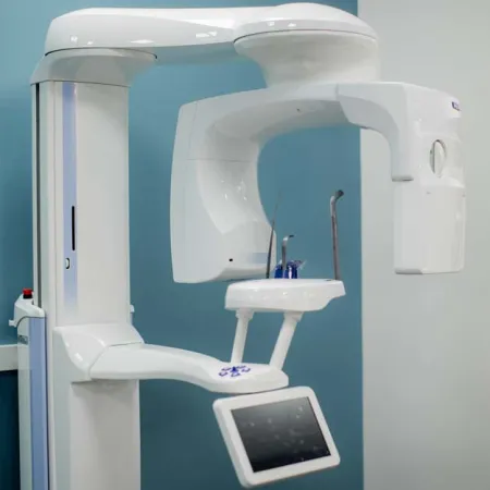 White dental panoramic X-ray machine with control panel in a clean clinic room with blue walls.