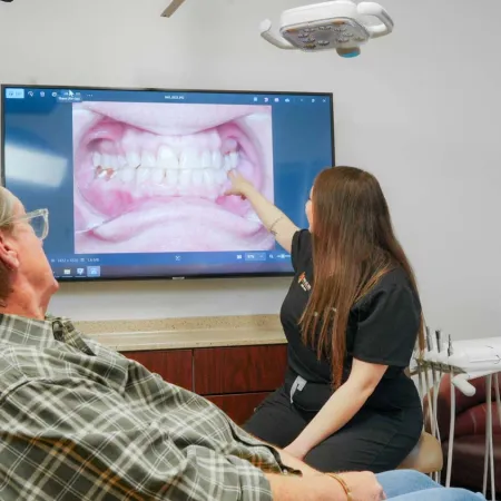 Dental professional shows patient images of teeth and gums on a screen during a dental consultation.