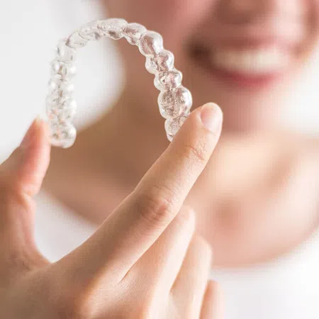 Person holding a clear dental aligner, showcasing its design and application.