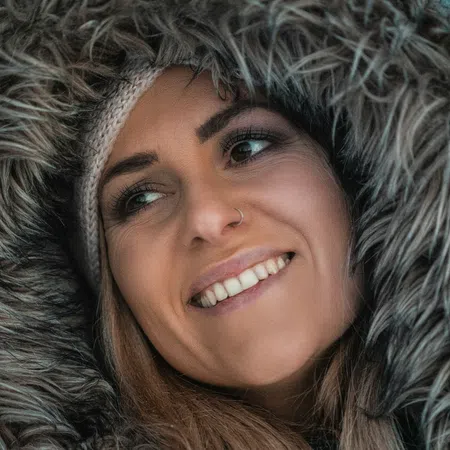 Smiling woman wearing a fur-lined hood and knit beanie in a close-up winter portrait.