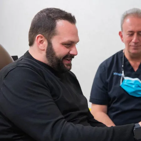 Man discussing treatment options with a male healthcare professional wearing scrubs and a face mask around his neck.