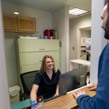 Smiling receptionist in black scrubs attending to male visitor at medical office front desk