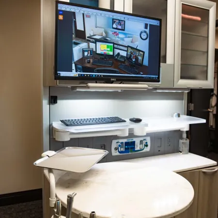 Modern dental operatory with computer monitor, dental tools, and workspace with keyboard and mouse.