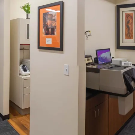 Modern office hallway with framed artwork, carpeted floors, and a workstation with computer and printer.