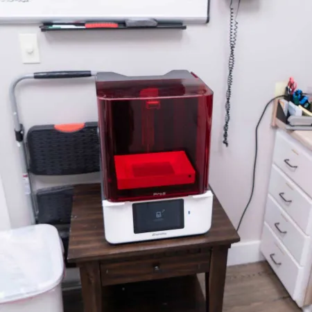 Formlabs Form 3 3D printer with red cover on wooden table in office workspace.