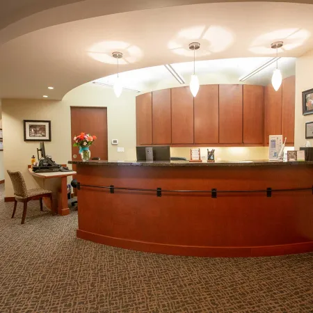 Reception area with curved wooden desk, pendant lights, carpeted floor, and framed artwork on beige walls