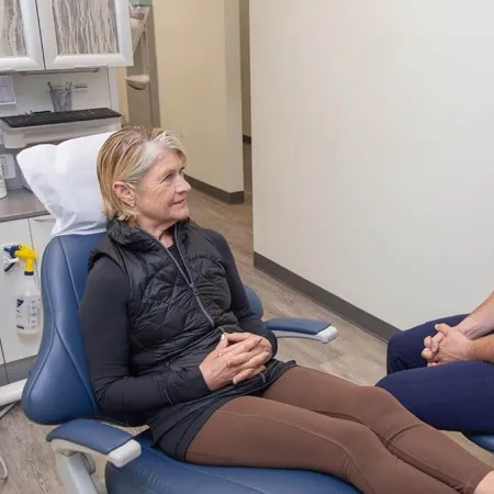 Female patient in a dental chair consulting with a smiling male dentist in navy scrubs in a clinic room