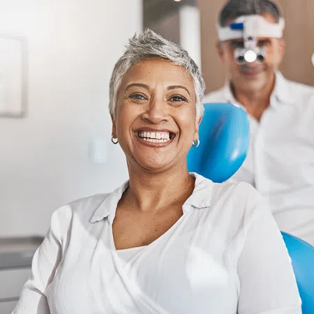 Smiling woman in dental chair with a dentist preparing for an appointment in a modern clinic.