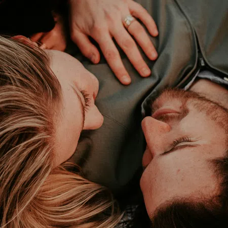 Close-up of a couple lying down facing each other, showing affection and intimacy with a hand resting gently.