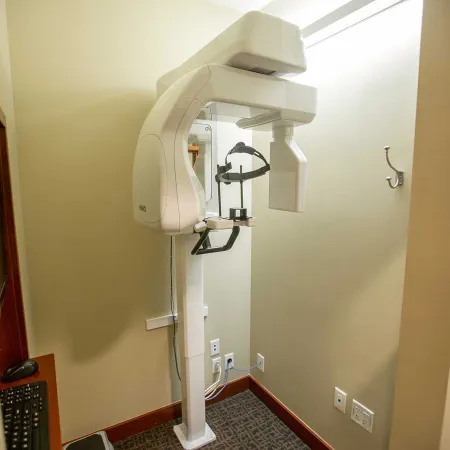 Modern panoramic dental X-ray machine in a clean, small beige examination room with computer controls.