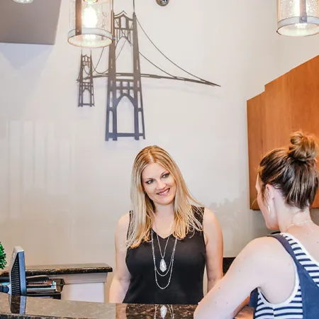 A friendly receptionist welcomes a visitor at a stylish office front desk with modern decor.
