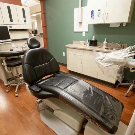 Modern dental office with black reclining patient chair, dental tools, and cabinetry on wood floors