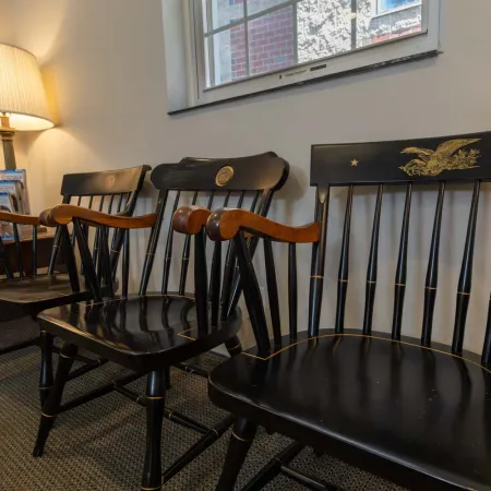 Row of vintage wooden chairs with black finish and armrests in a cozy room with lamp and window light.