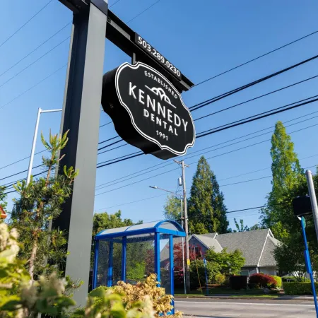 Kennedy Dental black and white hanging sign on a pole by a street with trees and houses in background