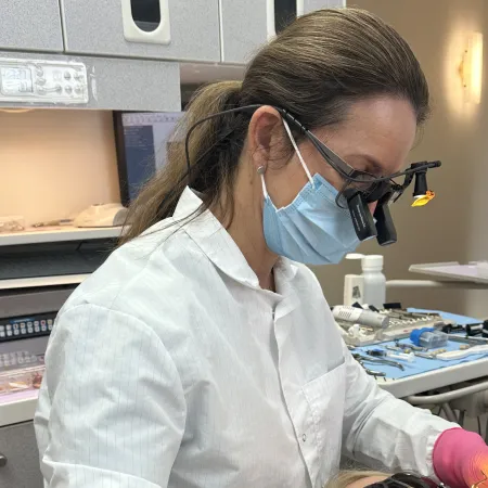 Female dentist wearing magnifying glasses and mask working on a dental patient in a modern clinic.