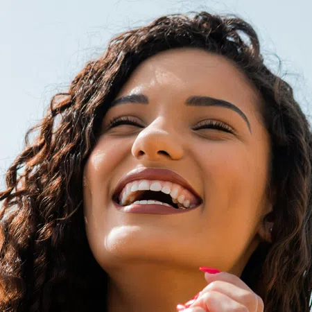 A cheerful woman with curly hair and a bright smile, enjoying a sunny day outdoors.