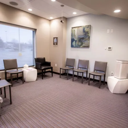 Modern waiting room with chairs, artwork, large window, and neutral color tones, featuring magazines and air purifier.