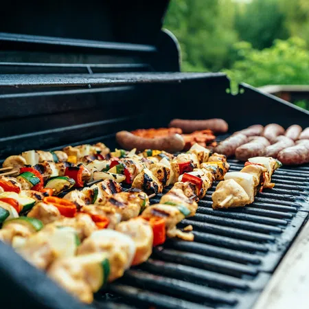 Grilled chicken and vegetable skewers with sausages cooking on an outdoor gas grill on a sunny day