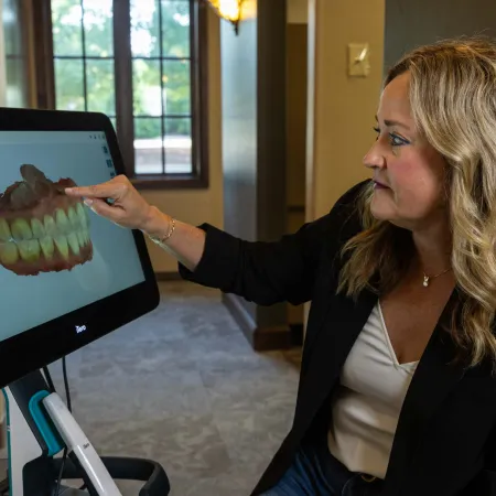 Woman pointing at 3D digital dental image on a large screen in a modern office setting.