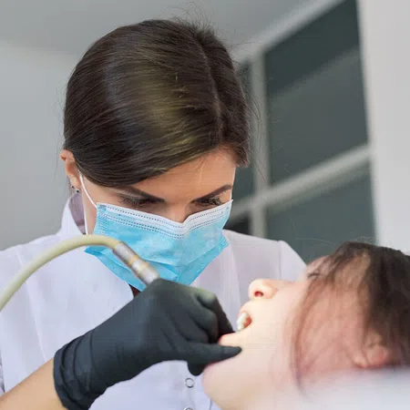 A dentist in a mask examines a patient's teeth during a dental check-up.