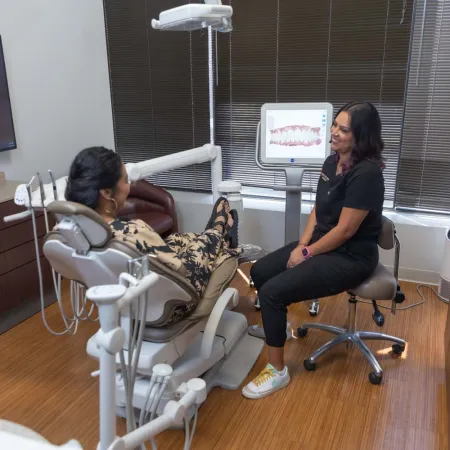 Dentist consulting patient in modern dental office with digital teeth imaging on screen and dental chair.