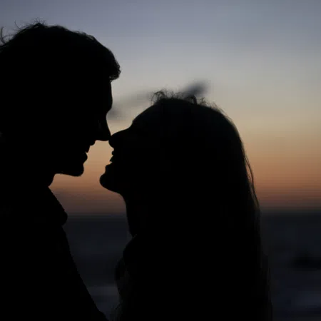 Silhouetted couple facing each other closely at sunset by the beach, creating a romantic atmosphere.